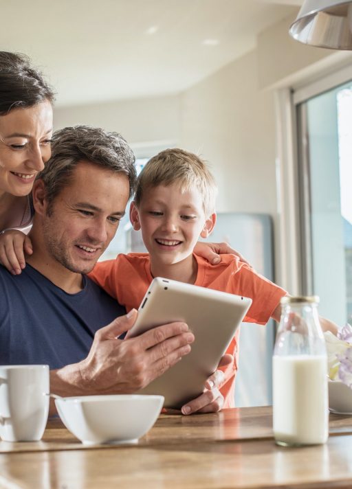 A modern family using a digital tablet while having breakfast in the kitchen, mom,  dad and their eight year old son